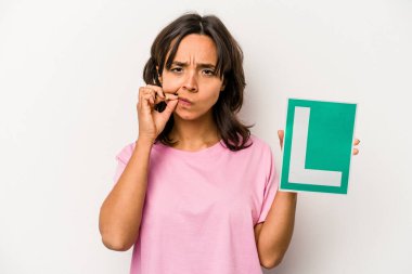 Genç İspanyol kadın acemi sürücü tabelasını tutuyor. Beyaz arka planda izole edilmiş, parmakları dudaklarında bir sır saklıyor..