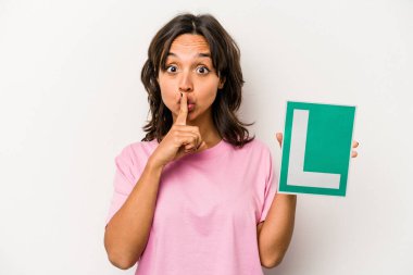 Genç İspanyol kadın elinde acemi sürücü tabelası tutuyor beyaz arka planda izole edilmiş bir şekilde ya sır saklıyor ya da sessizlik istiyor..