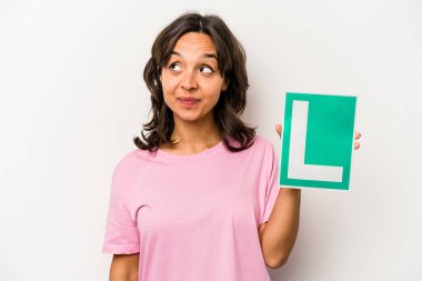 Beyaz arka planda izole edilmiş acemi sürücü tabelasını tutan genç İspanyol kadın gülümsüyor, neşeli ve keyifli görünüyor..