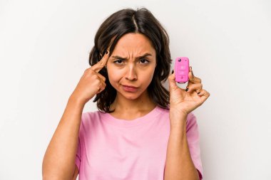 Beyaz arka planda izole edilmiş araba anahtarlarını tutan genç İspanyol kadın şakağı parmağıyla işaret ediyor, düşünüyor ve bir göreve odaklanıyor..