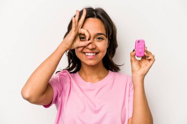 Beyaz arka planda izole edilmiş araba anahtarlarını tutan genç İspanyol kadın heyecanlı..