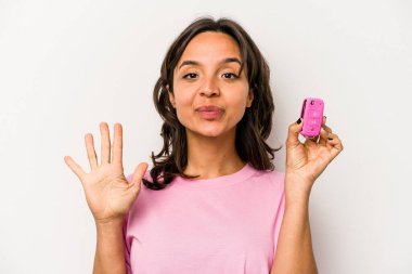 Beyaz arka planda izole edilmiş araba anahtarlarını tutan genç İspanyol kadın gülümseyerek beş numarayı parmaklarıyla gösteriyor..