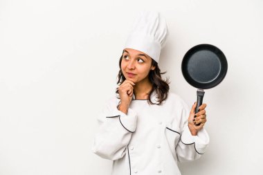 Beyaz arka planda izole edilmiş genç İspanyol aşçı kadın şüpheli ve şüpheci bir ifadeyle yana bakıyor..
