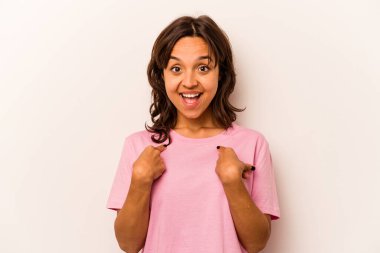 Beyaz arka planda izole edilmiş genç İspanyol kadın parmağını göstererek şaşırdı, geniş bir gülümsemeyle..