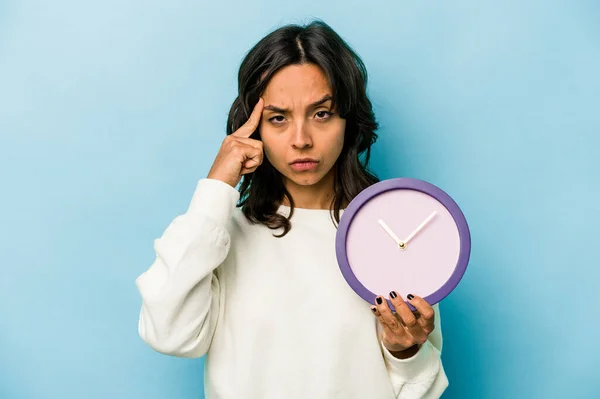 Young Hispanic Woman Holding Clock Isolated Blue Background Pointing Temple — Stockfoto