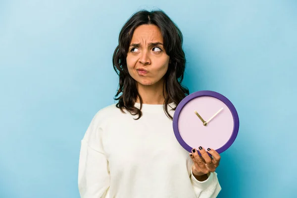 Young Hispanic Woman Holding Clock Isolated Blue Background Confused Feels — Foto de Stock