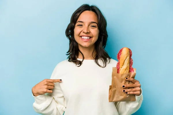 Young Hispanic Woman Eating Sandwich Isolates Blue Background Person Pointing — Stockfoto