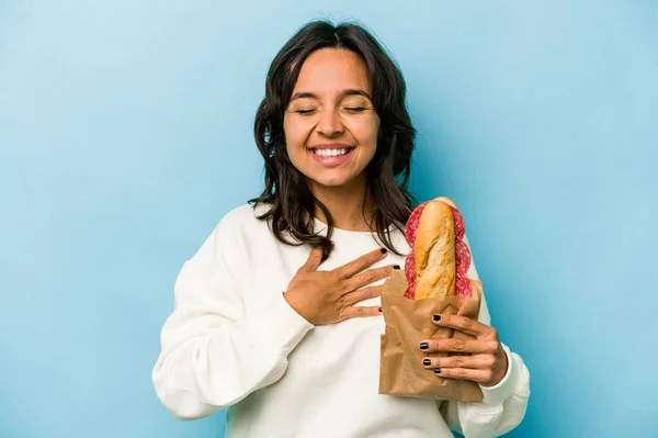 Young Hispanic Woman Eating Sandwich Isolates Blue Background Laughs Out — Photo