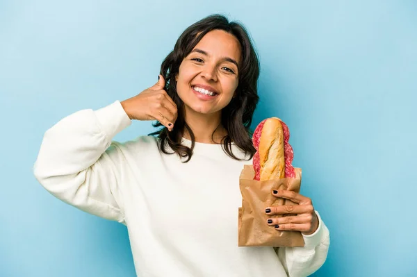 Young Hispanic Woman Eating Sandwich Isolates Blue Background Showing Mobile — Stockfoto