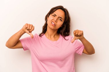 Beyaz arka planda izole edilmiş genç İspanyol kadın baş parmağını aşağı gösteriyor ve hoşlanmadığını ifade ediyor..