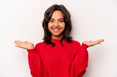 Beyaz arka planda izole edilmiş genç İspanyol kadın kollarıyla ölçeği yapıyor, mutlu ve kendinden emin hissediyor..