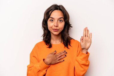 Beyaz arka planda izole edilmiş genç İspanyol kadın yemin ediyor, elini göğsüne koyuyor..