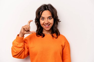 Beyaz arka planda izole edilmiş genç İspanyol kadın işaret parmaklarıyla küçük bir şey tutuyor, gülümsüyor ve kendinden emin..