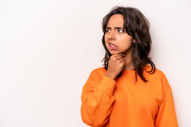 Beyaz arka planda izole edilmiş genç İspanyol kadın kafasının arkasına dokunuyor, düşünüyor ve bir seçim yapıyor..