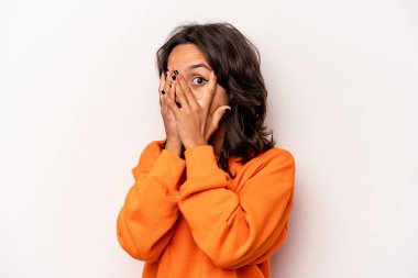 Beyaz arka planda izole edilmiş genç İspanyol kadın parmaklarının arasından korkmuş ve gergin bir şekilde göz kırpıyor..