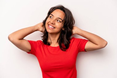 Beyaz arka planda izole edilmiş genç bir İspanyol kadın kendini güvende hissediyor, elleri başının arkasında..