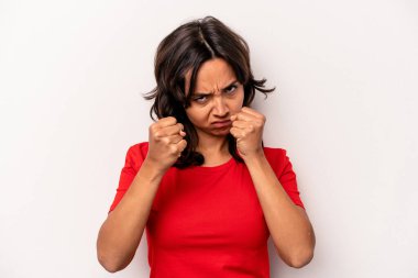 Beyaz arka planda izole edilmiş genç İspanyol kadın kameraya yumruk gösteriyor, agresif yüz ifadesi..