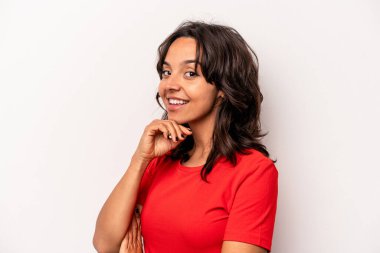 Beyaz arka planda izole edilmiş genç İspanyol kadın gülümsüyor ve kendinden emin, elleriyle çenesine dokunuyor..