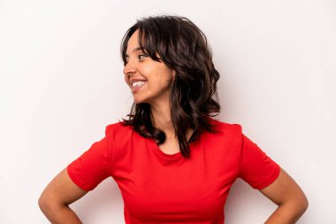 Beyaz arka planda izole edilmiş genç İspanyol kadın mutlu bir şekilde gülüyor ve ellerini karnının üstünde tutarak eğleniyor..