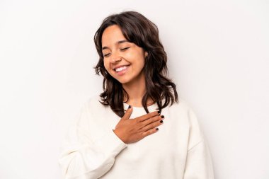 Beyaz arka planda izole edilmiş genç İspanyol kadın gülüyor, ellerini kalbe koyuyor, mutluluk kavramını koruyor..