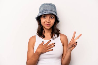 Beyaz arka planda izole edilmiş genç İspanyol kadın yemin ediyor, elini göğsüne koyuyor..