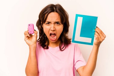 Latin kökenli genç bir kadın elinde başlangıç levhası ve mavi arka planda izole edilmiş anahtar bir araba tutuyor.