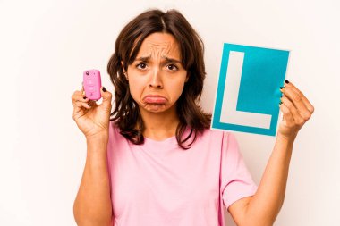 Latin kökenli genç bir kadın elinde başlangıç levhası ve mavi arka planda izole edilmiş anahtar bir araba tutuyor.