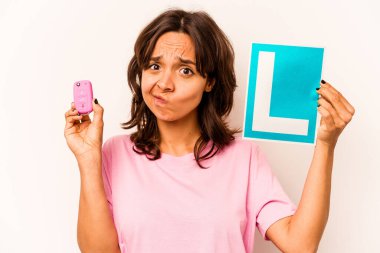 Latin kökenli genç bir kadın elinde başlangıç levhası ve mavi arka planda izole edilmiş anahtar bir araba tutuyor.