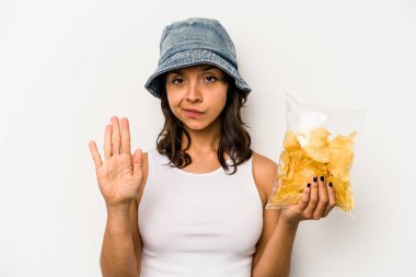 Beyaz arka planda izole edilmiş bir paket cipsi tutan genç İspanyol kadın elini uzatmış, dur işaretini göstererek seni engelliyor..