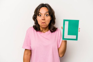 Genç bir İspanyol kadının elinde acemi sürücü işareti var. Beyaz arka planda izole edilmiş omuz silkiyor ve gözleri açık..