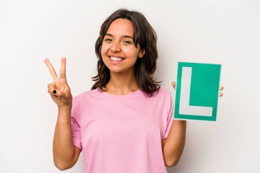 Genç İspanyol kadın elinde acemi sürücü tabelası tutuyordu. Beyaz arka planda iki numarayı parmaklarıyla gösteriyordu..