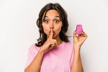 Beyaz arka planda izole edilmiş araba anahtarlarını tutan genç İspanyol kadın ya sır saklıyor ya da sessizlik istiyor..