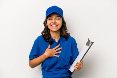 Beyaz arka planda izole edilmiş genç İspanyol kadın teslimatçı elini göğsünde tutarak kahkaha atıyor..