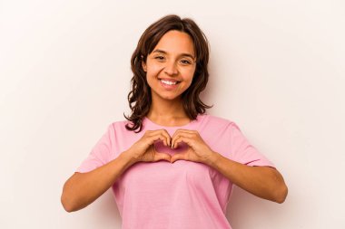 Beyaz arka planda izole edilmiş genç İspanyol kadın gülümsüyor ve elleriyle kalp şeklini gösteriyor..