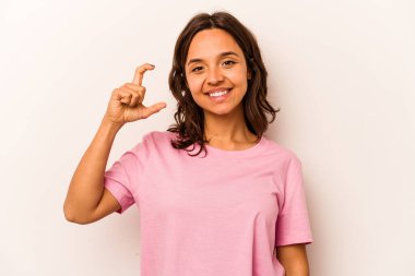 Beyaz arka planda izole edilmiş genç İspanyol kadın işaret parmaklarıyla küçük bir şey tutuyor, gülümsüyor ve kendinden emin..