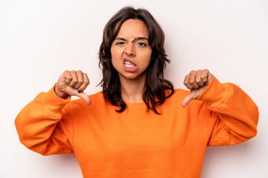 Beyaz arka planda izole edilmiş genç İspanyol kadın baş parmağını aşağı gösteriyor ve hoşlanmadığını ifade ediyor..