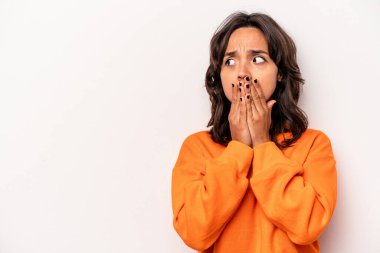 Latin kökenli genç bir kadın beyaz arka planda izole edilmiş. Düşünceli bir şekilde bir fotokopi odasına bakıyor. Ağzını eliyle kapatıyor..