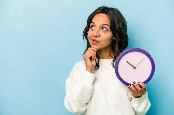 Young Hispanic Woman Holding Clock Isolated Blue Background Looking Sideways — Stok fotoğraf