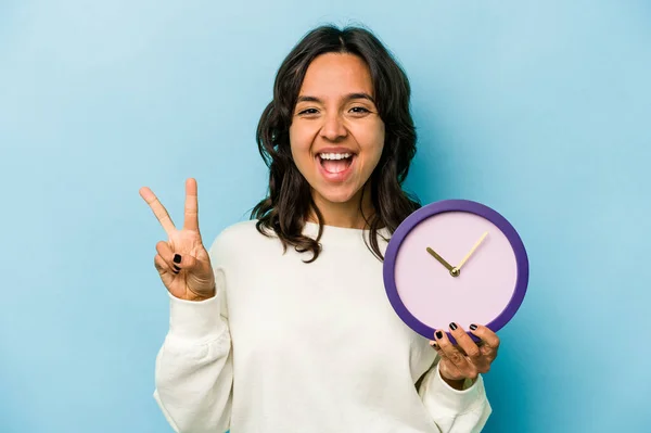 Young Hispanic Woman Holding Clock Isolated Blue Background Showing Number — Stok fotoğraf