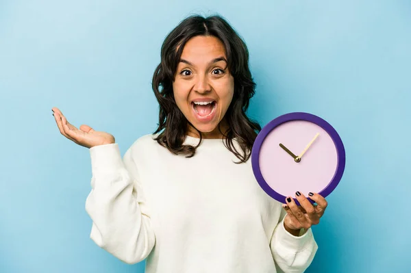 Young Hispanic Woman Holding Clock Isolated Blue Background Receiving Pleasant — Stok fotoğraf