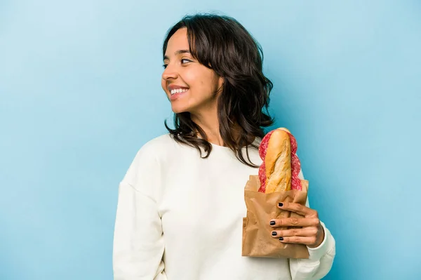 Young Hispanic Woman Eating Sandwich Isolates Blue Background Looks Aside — Stockfoto