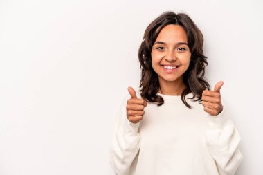 Beyaz arka planda izole edilmiş genç İspanyol kadın gülümsüyor ve başparmağını kaldırıyor.