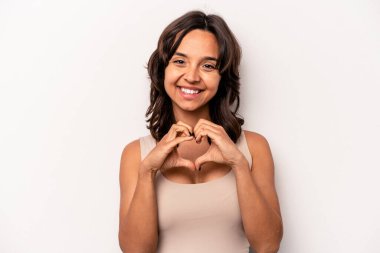 Beyaz arka planda izole edilmiş genç İspanyol kadın gülümsüyor ve elleriyle kalp şeklini gösteriyor..