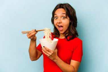 Young hispanic woman eating noodles isolated on blue background