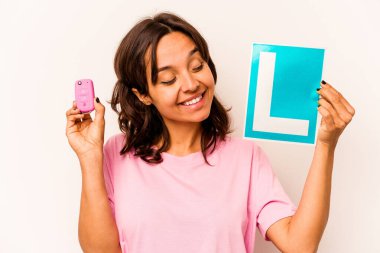 Latin kökenli genç bir kadın elinde başlangıç levhası ve mavi arka planda izole edilmiş anahtar bir araba tutuyor.