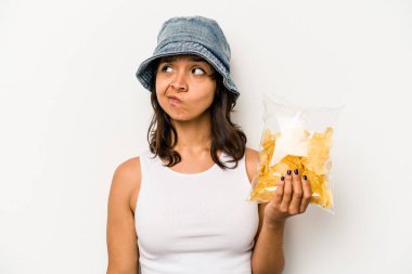 Beyaz arka planda izole edilmiş bir paket cipsi tutan genç İspanyol kadın kafası karışmış, şüpheli ve güvensiz hissediyor..