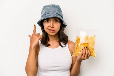 Beyaz arka planda izole edilmiş bir paket cipsi tutan genç İspanyol kadın işaret parmağıyla yaptığı hayal kırıklığı jestini gösteriyor..