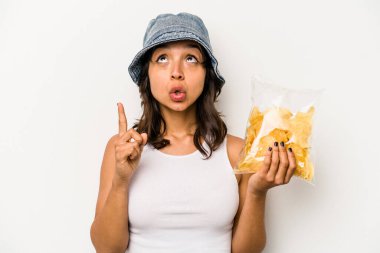 Beyaz arka planda izole edilmiş bir paket cipsi tutan genç İspanyol kadın ağzı açık bir şekilde üst tarafı işaret ediyor..