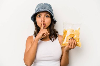 Beyaz arka planda izole edilmiş bir paket cipsi tutan genç İspanyol kadın bir sır saklıyor ya da sessizlik istiyor..