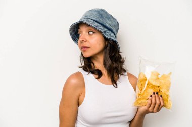 Beyaz arka planda izole edilmiş bir paket cipsi tutan genç İspanyol kadın gülümsüyor ve keyifli görünüyor..